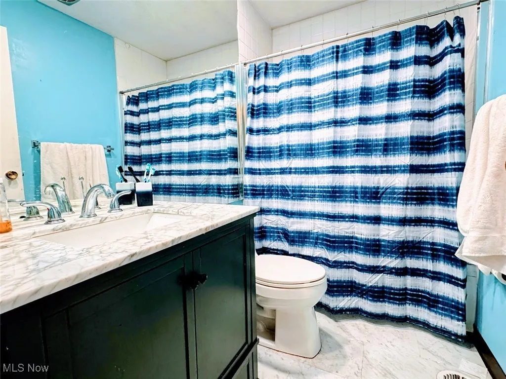 Bathroom with vanity, toilet, marble finish flooring, and a shower with curtain