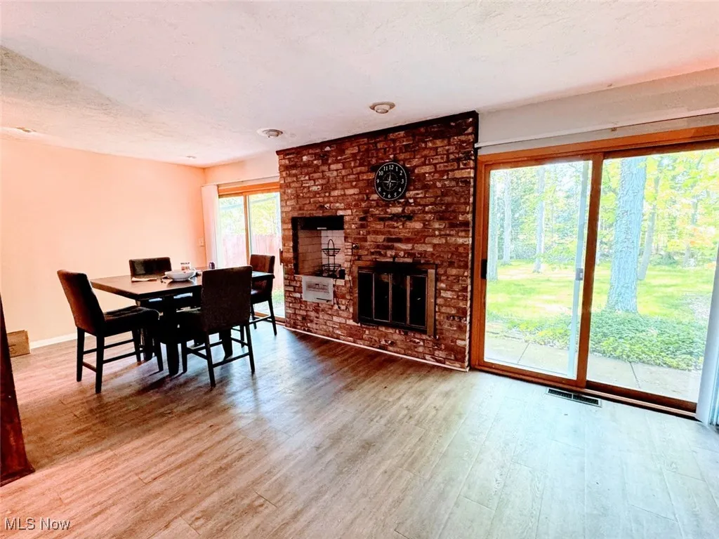 Dining room featuring wood finished floors, baseboards, a brick fireplace, and a textured ceiling