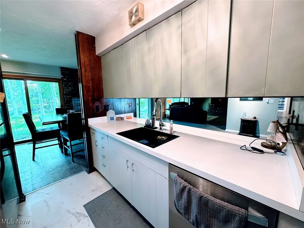 Kitchen with a sink, light marble finish flooring, dishwasher, light countertops, and modern cabinets