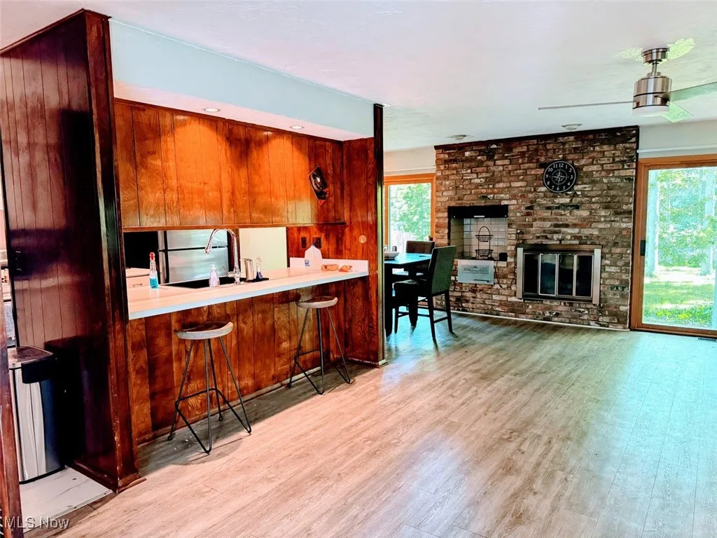 Kitchen with wood finished floors, a brick fireplace, brown cabinets, a breakfast bar, and light countertops