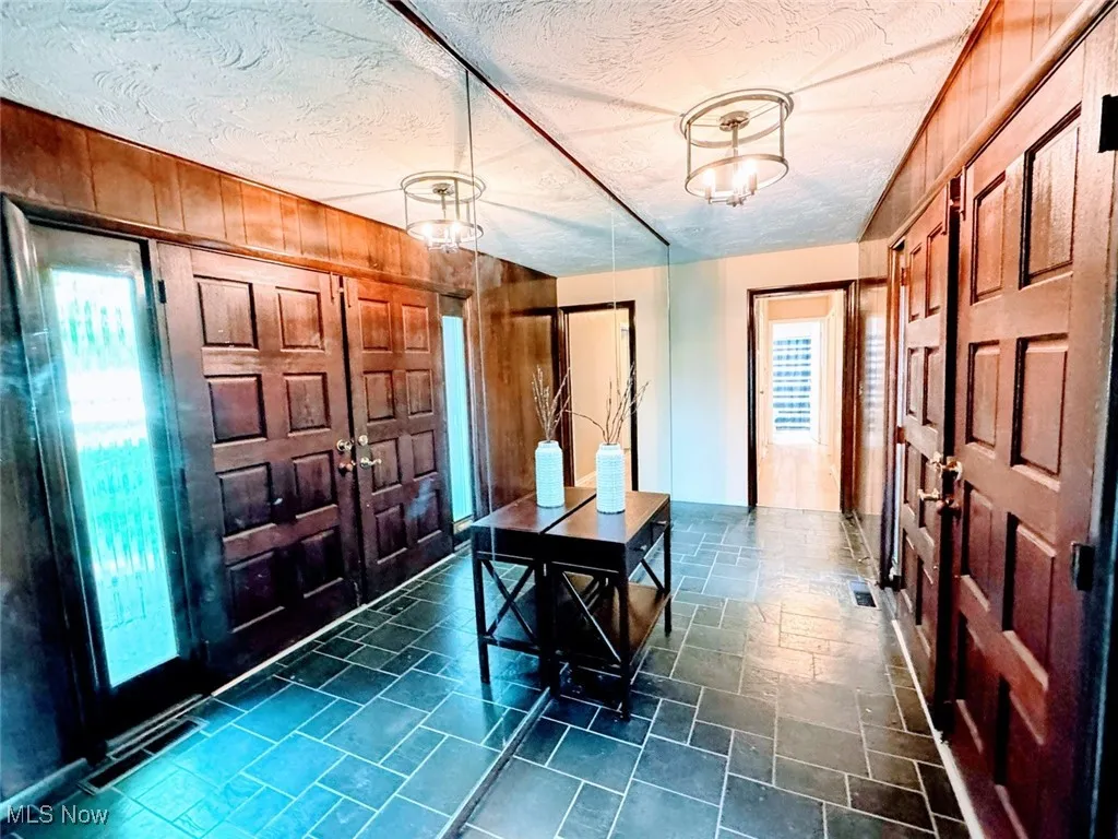 Entryway with a chandelier, wood walls, stone tile flooring, and a textured ceiling