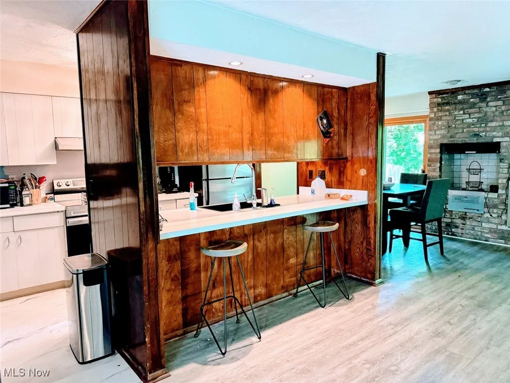 Kitchen with stainless steel electric range, a sink, light wood-type flooring, a kitchen bar, and under cabinet range hood