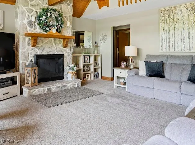 Living area with carpet floors, a stone fireplace, baseboards, and vaulted ceiling