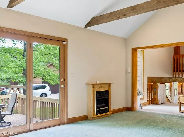 Unfurnished living room featuring carpet floors, vaulted ceiling, a glass covered fireplace, and baseboards