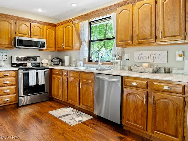 Kitchen featuring appliances with stainless steel finishes, a sink, light countertops, brown cabinets, and recessed lighting