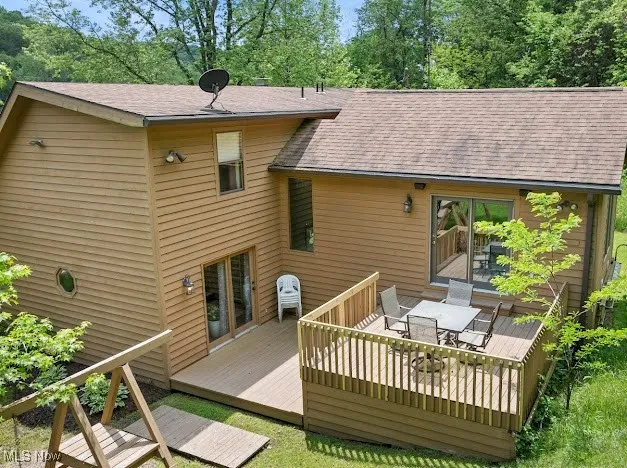 Rear view of house featuring outdoor dining space, a wooden deck, and roof with shingles