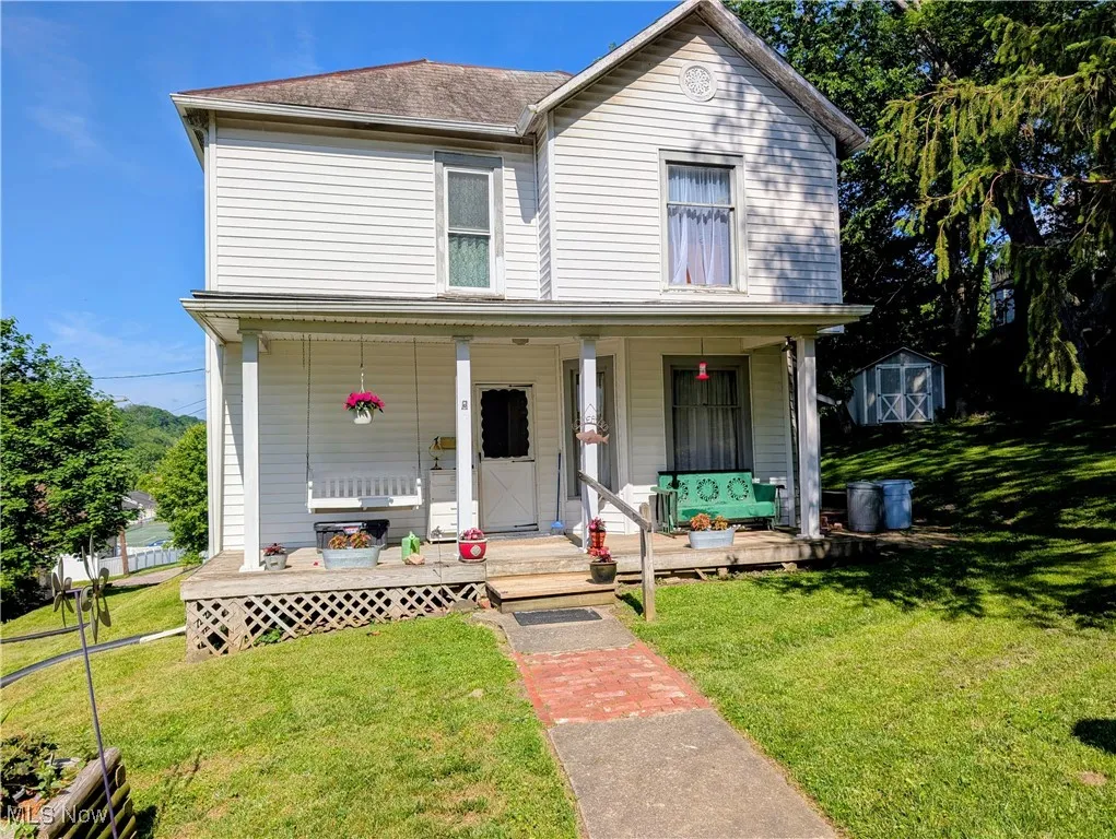 View of front of property with covered porch, a storage unit, a front yard, and an outbuilding