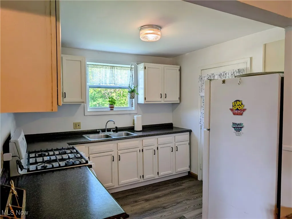 Kitchen featuring freestanding refrigerator, a sink, dark countertops, white cabinets, and dark wood finished floors