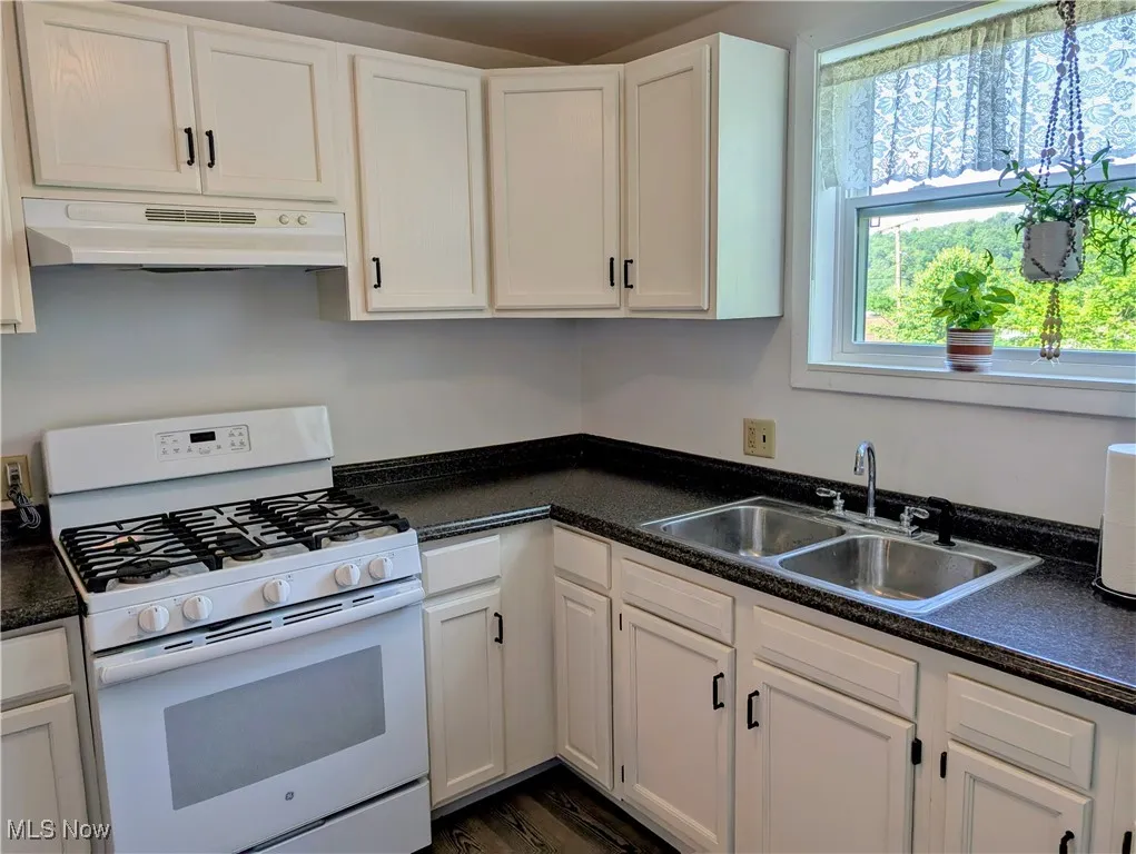 Kitchen with gas range gas stove, under cabinet range hood, a sink, and white cabinetry