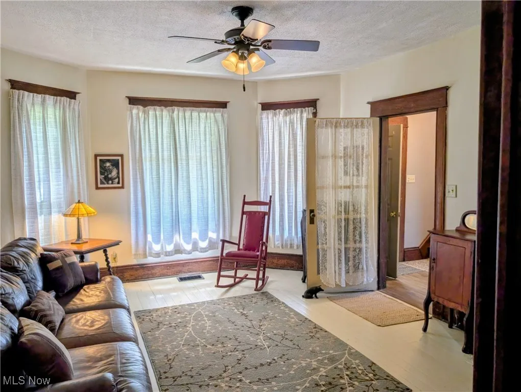 Living area featuring a ceiling fan, healthy amount of natural light, a textured ceiling, and wood finished floors