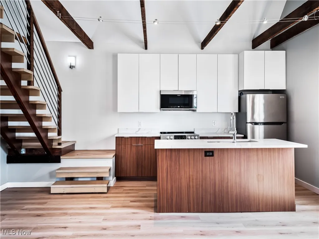 Kitchen featuring appliances with stainless steel finishes, beam ceiling, an island with undermount sink, and quartz countertops