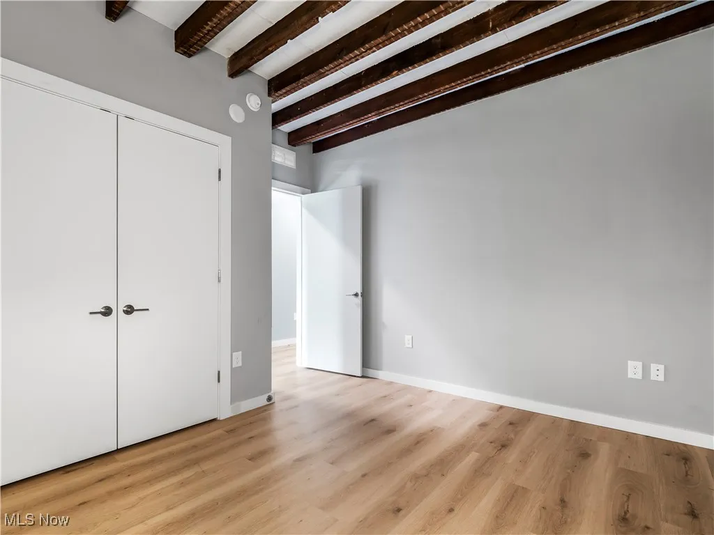 Bedroom featuring beam ceiling, light wood finished floors, baseboards, and a closet