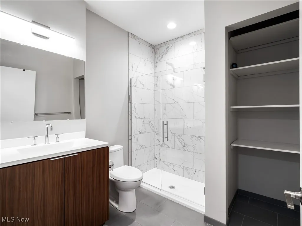 Full bathroom with toilet, marble walk-in shower, vanity, and tile patterned flooring