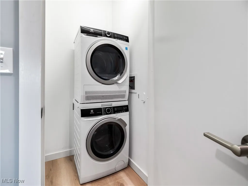In unit laundry room featuring stacked washer and dryer, light wood finished floors, and baseboards