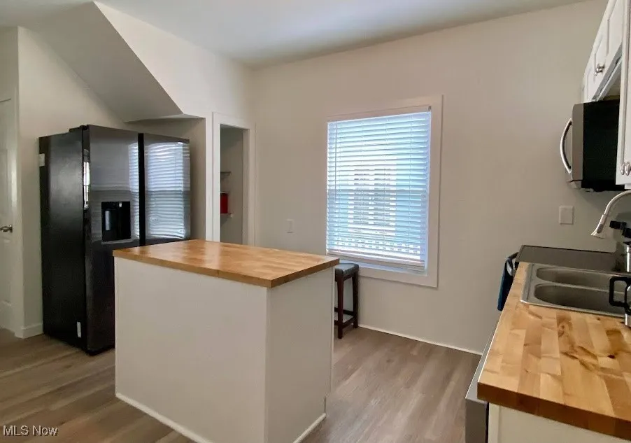 Kitchen with wood counters, stainless steel microwave, black refrigerator with ice dispenser, light wood finished floors, and white cabinets