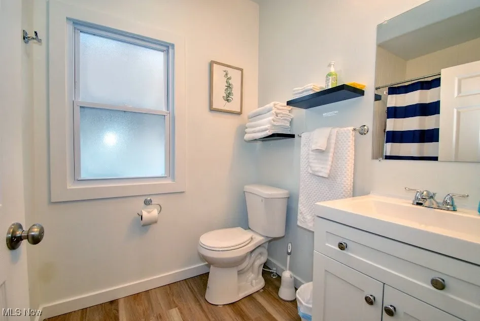 Bathroom with baseboards, wood finished floors, toilet, vanity, and curtained shower