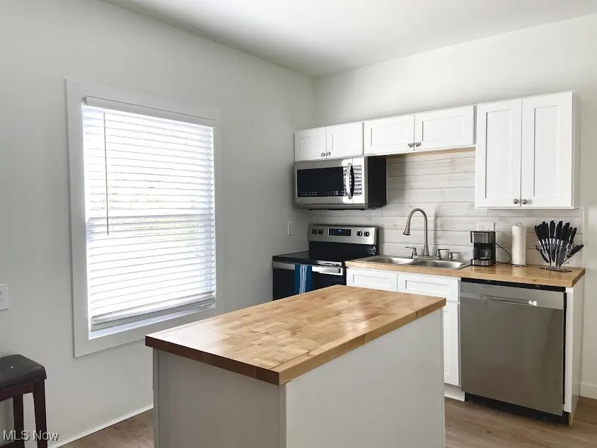 Kitchen with wooden counters, stainless steel appliances, a sink, and wood finished floors