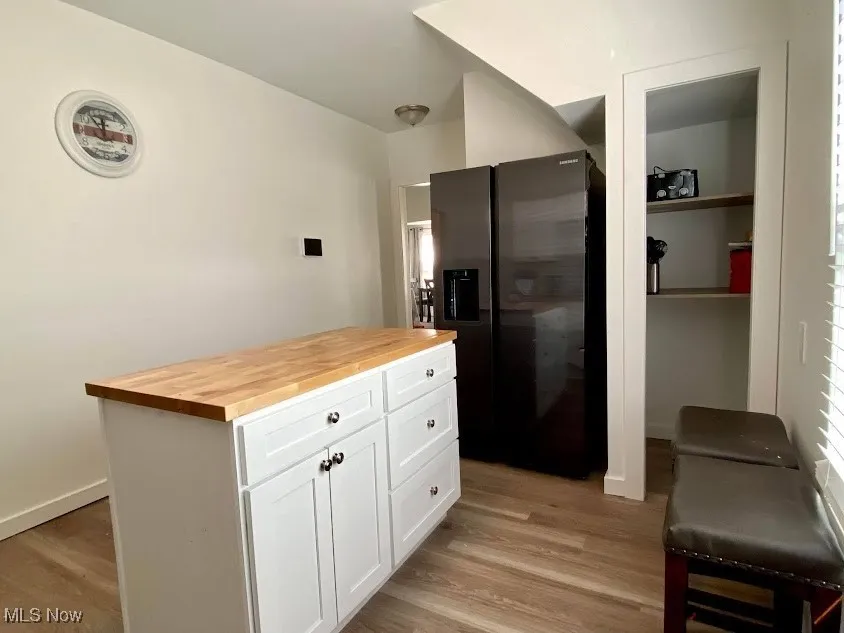 Kitchen with wooden counters, fridge with ice dispenser, white cabinets, light wood-type flooring, and a center island