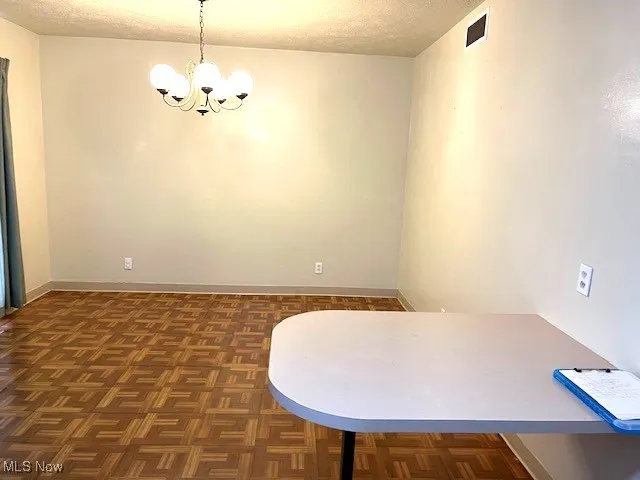 Unfurnished dining area with a chandelier, a textured ceiling, and baseboards