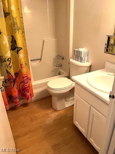Full bathroom with wood finished floors, shower / bath combo with shower curtain, toilet, and vanity