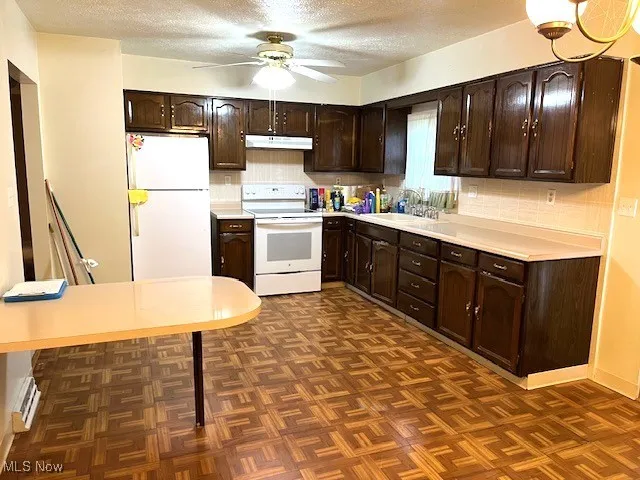 Kitchen with white appliances, under cabinet range hood, dark brown cabinets, a textured ceiling, and a sink