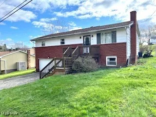 Back of property featuring brick siding, a chimney, an attached garage, asphalt driveway, and a lawn