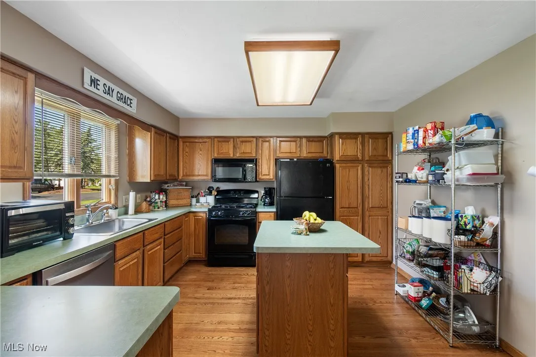 Kitchen featuring black appliances, a sink, light wood finished floors, light countertops, and brown cabinetry