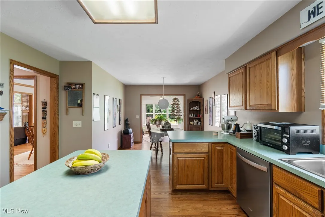 Kitchen featuring stainless steel dishwasher, light wood-style flooring, a peninsula, brown cabinetry, and light countertops