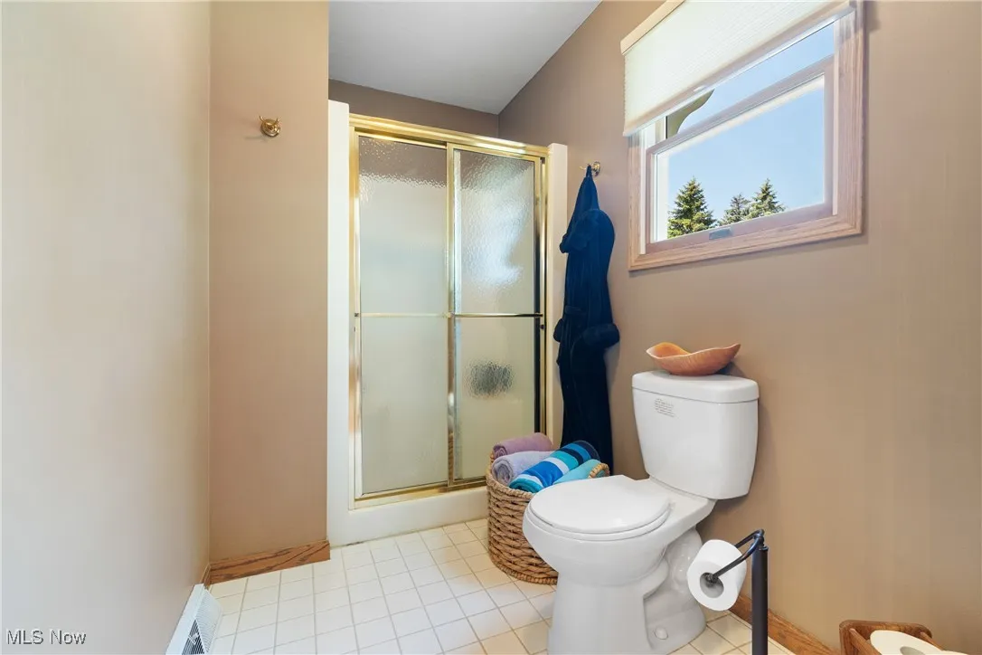 Full bath with a stall shower, toilet, tile patterned flooring, and baseboards