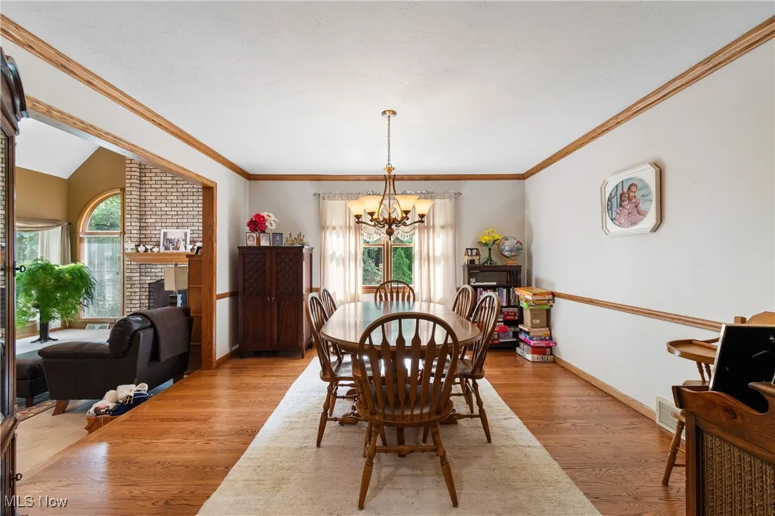 Dining area featuring a chandelier, wood finished floors, baseboards, a fireplace, and crown molding