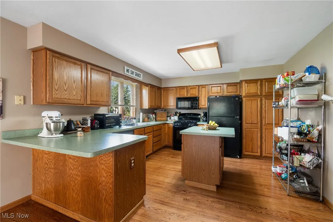 Kitchen with black appliances, a sink, a peninsula, brown cabinets, and light wood-type flooring