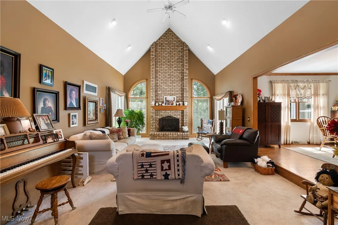 Carpeted living room featuring high vaulted ceiling, a ceiling fan, healthy amount of natural light, and a brick fireplace