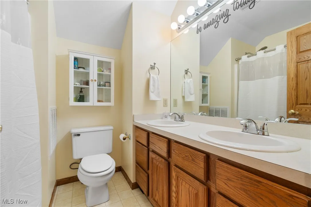 Full bathroom with lofted ceiling, toilet, double vanity, baseboards, and tile patterned flooring