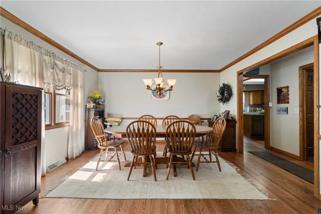 Dining room with a chandelier, wood finished floors, baseboards, and ornamental molding