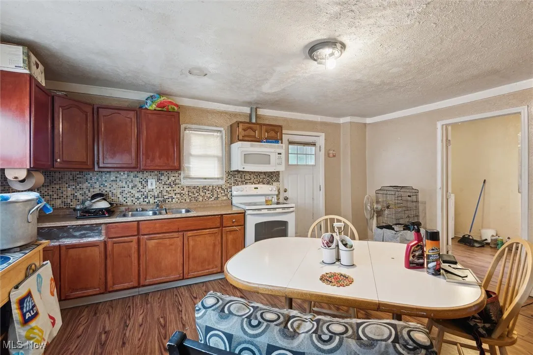 Kitchen with white appliances, wood finished floors, a sink, a textured ceiling, and light countertops