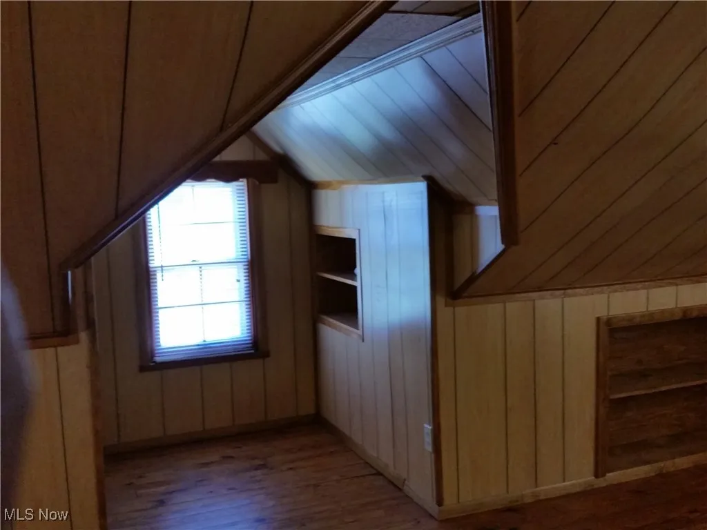 Additional living space with vaulted ceiling, wood finished floors, and wooden walls