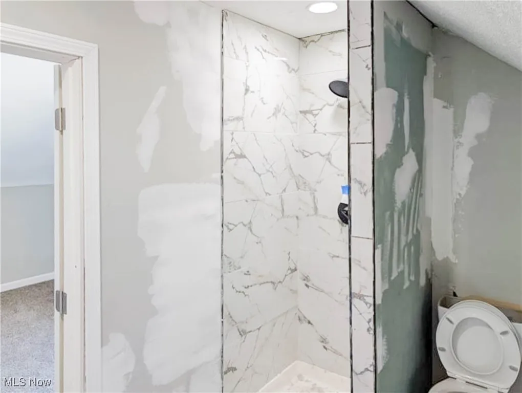 Full bathroom with a marble finish shower and toilet