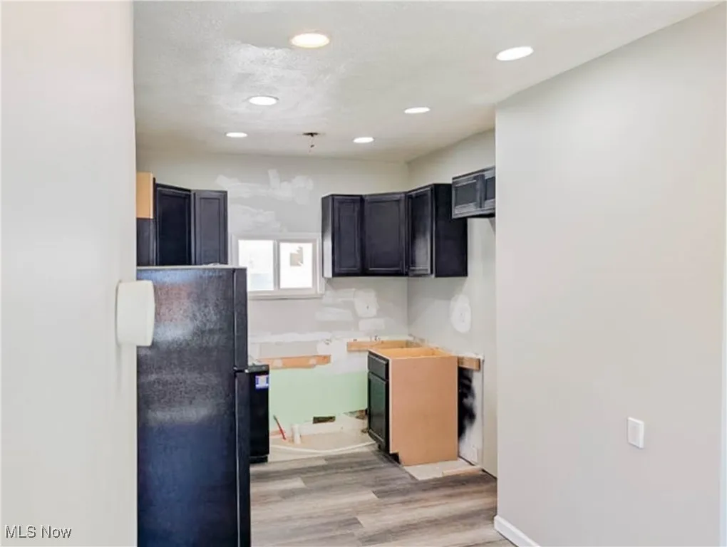 Kitchen featuring freestanding refrigerator, light wood finished floors, dark cabinetry, and recessed lighting