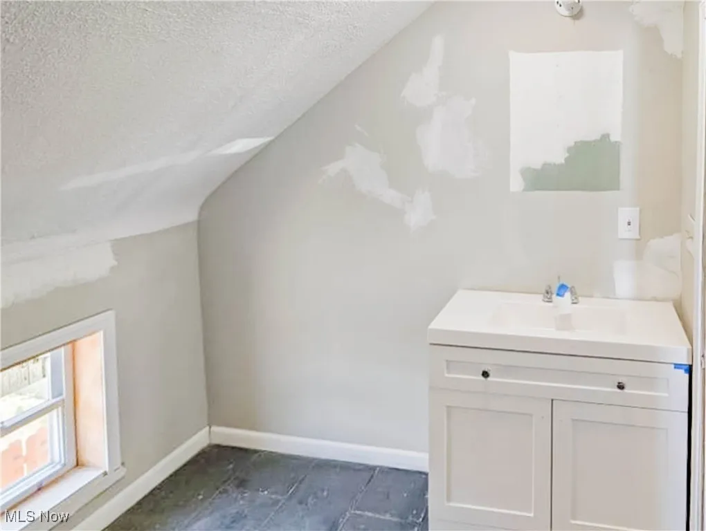Additional living space featuring a textured ceiling, baseboards, a sink, and lofted ceiling