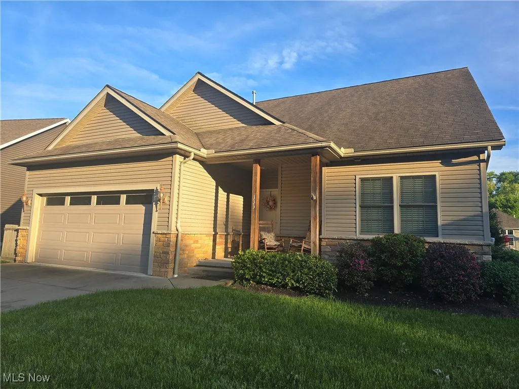 View of front of house featuring a garage, concrete driveway, a front yard, roof with shingles, and stone wrap and vinyl siding