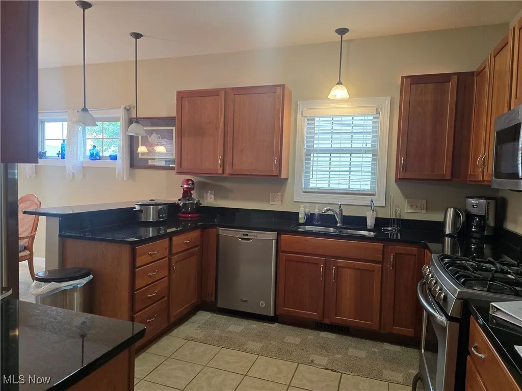 Kitchen with stainless steel appliances, a sink, a peninsula, light tile patterned flooring, and pendant lighting