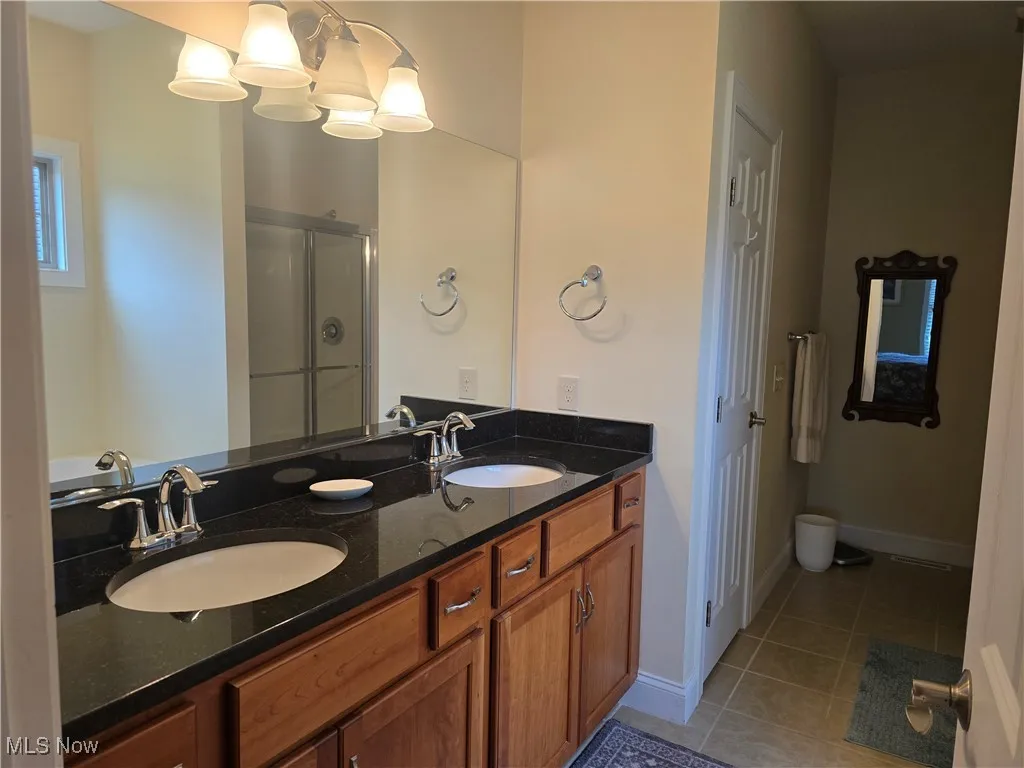 Bathroom with tile patterned flooring, a stall shower, double vanity, and baseboards