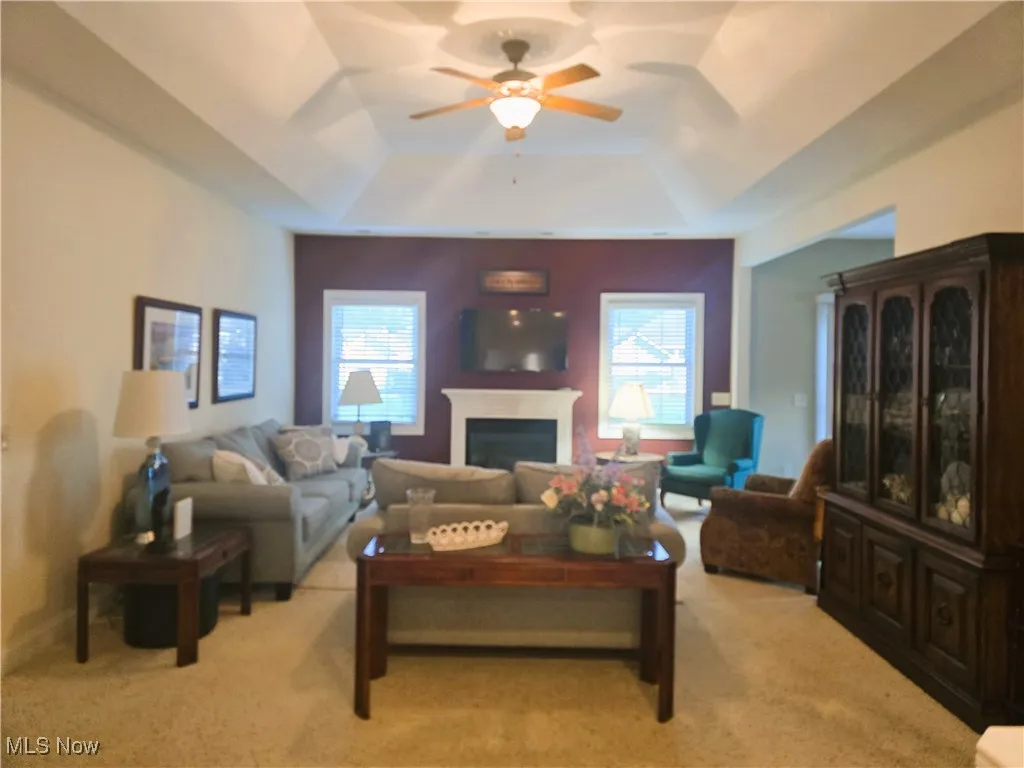 Living area featuring a tray ceiling, a ceiling fan, a gas fireplace, and light colored carpet