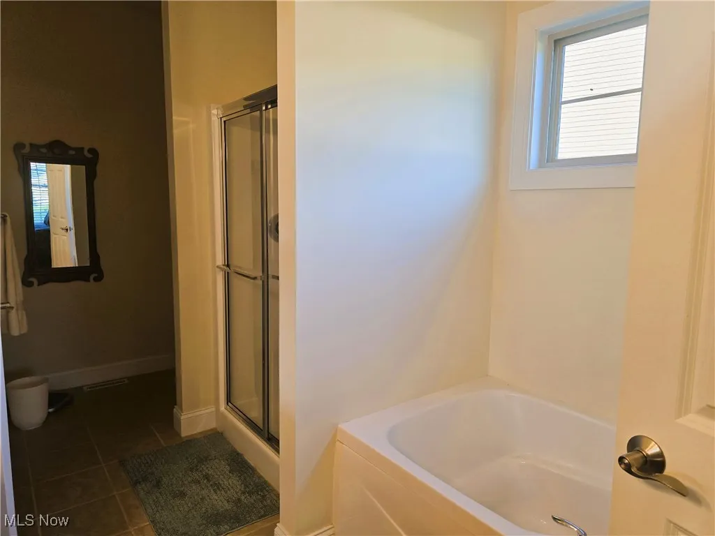 Full bath with tile patterned floors, a stall shower, a bath, double sinks.