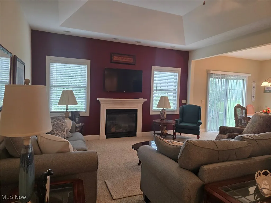 Living area with carpet flooring, a window surround the gas  fireplace, and baseboards