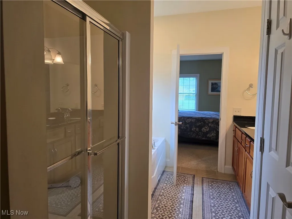 Bathroom featuring vanity, a garden tub, a shower stall, ensuite bath, and baseboards
