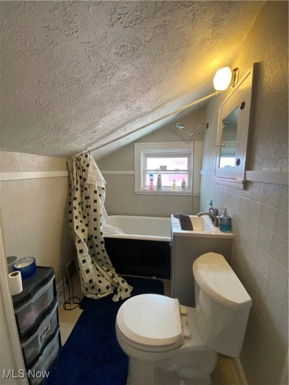 Bathroom featuring tile walls, a textured ceiling, vaulted ceiling, shower / bath combo, and vanity