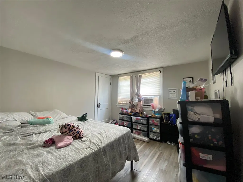 Bedroom with a textured ceiling, light wood finished floors, and cooling unit
