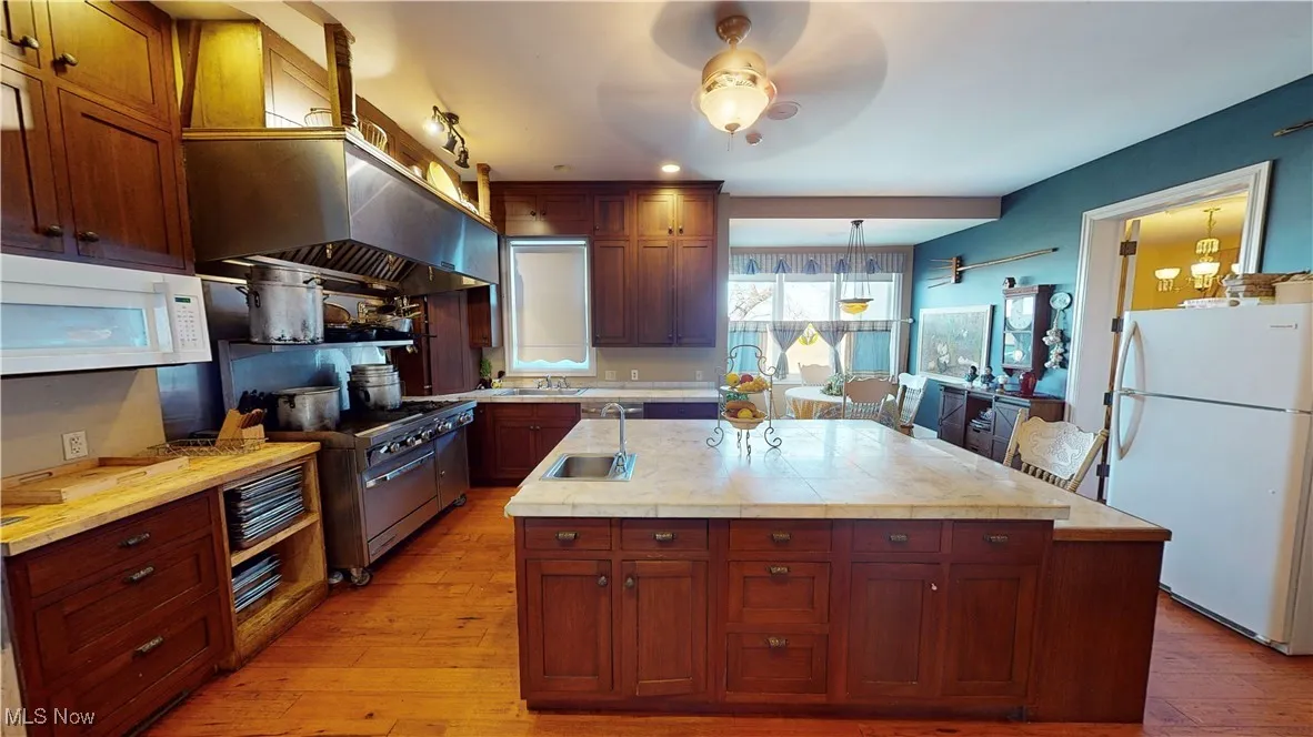 Kitchen with white appliances, a center island with sink, light hardwood / wood-style flooring, sink, and ceiling fan