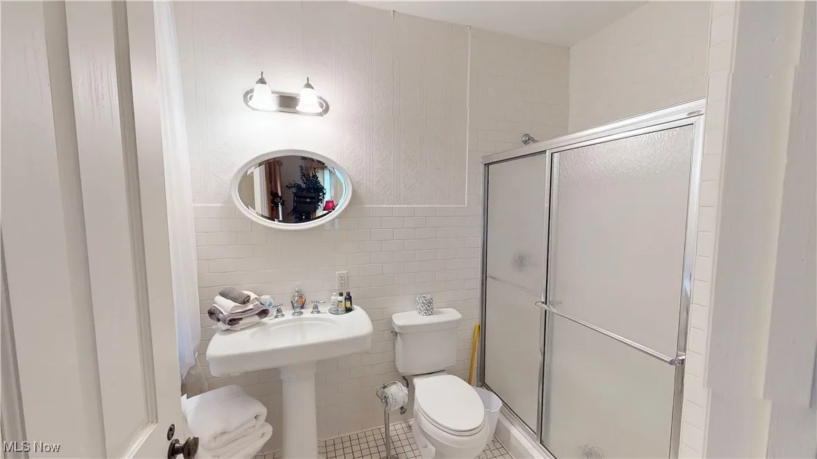 Bathroom with tile walls, toilet, a shower with shower door, and tile patterned floors